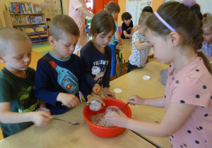 Dzieci nasypują łyżkami mieszankę soli z płatkami kwiatów do pojemników.